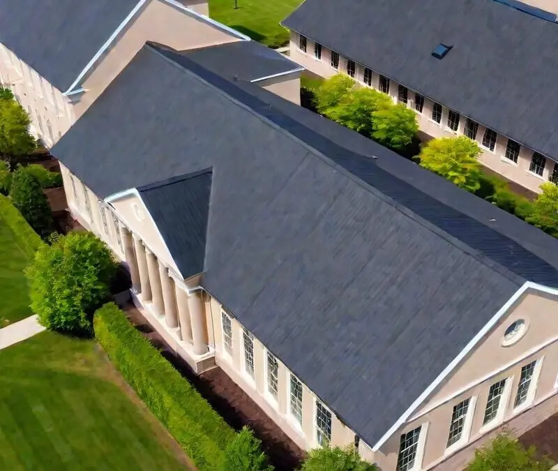 Aerial view of two beige buildings with dark gray roofs, surrounded by green lawns, trees, and walkways.