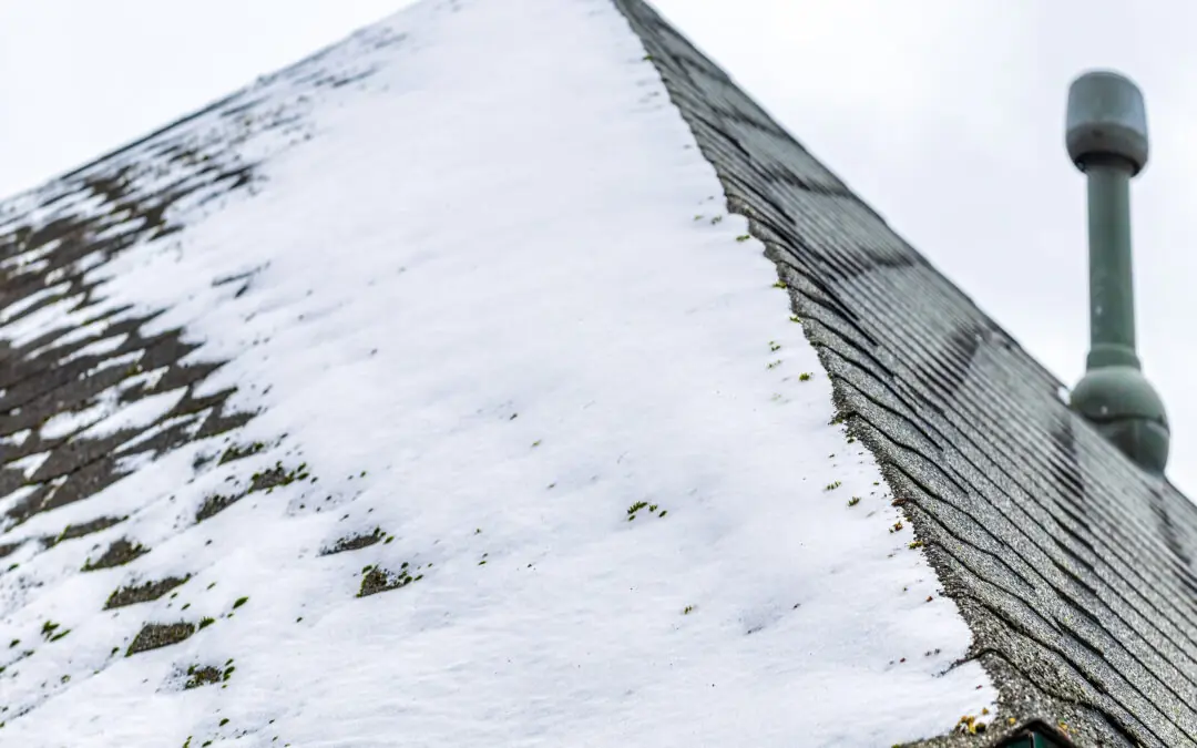 Close-up of a sloped roof partially covered in melting snow, with some shingles exposed and a vent pipe visible on the right side.