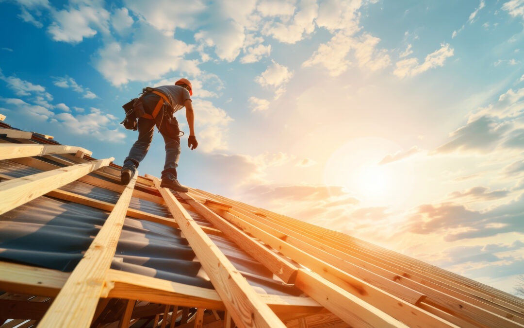 A construction worker wearing safety gear stands on a wooden roof frame under a bright sky with scattered clouds and sunlight.