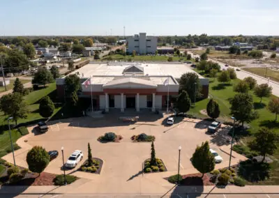 Aerial view of a large brick building with a parking lot and surrounding greenery. An American flag is visible near the entrance, highlighting Holthaus's expert roofing services discreetly integrated into the structure’s design.