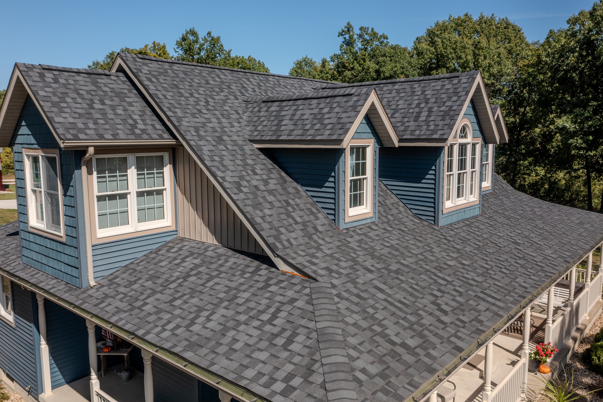 A completed Holthaus Roofing residential asphalt shingle roof with charcoal shingles, dormer windows and a wraparound porch on a central Illinois home