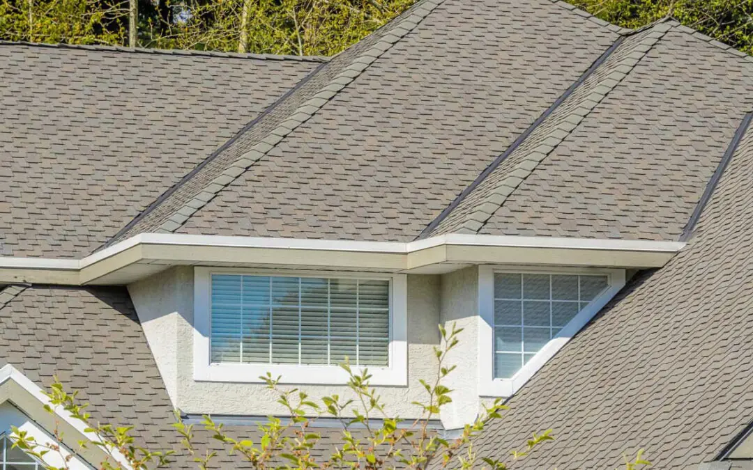 Close-up of a house roof with gray asphalt shingles and a dormer window, showcasing the expert craftsmanship of Holthaus roofing services.
